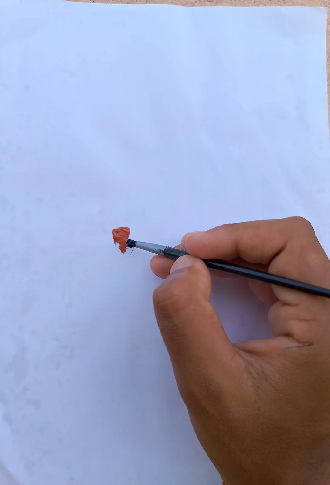 An artist's hand painting with a fine brush on white paper